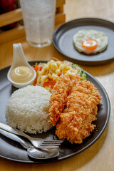 Fried fish steak with sausage dressing, rice and rosemary on black plate on wooden table.
