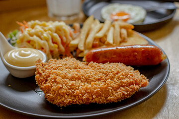 Fried fish steak with sausage dressing, rice and rosemary on black plate on wooden table.