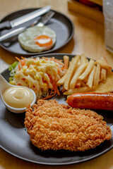 Fried fish steak with sausage dressing, rice and rosemary on black plate on wooden table.