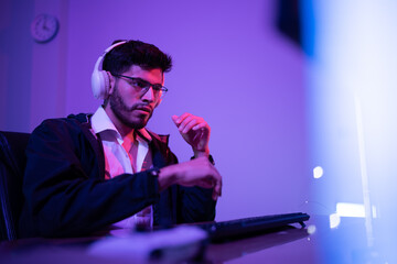 Focused man wearing headphones immersed in computer work at a dimly lit desk during the evening hours