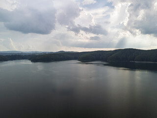 Aerial view of a tranquil lake surrounded by lush green forests under a cloudy sky, offering a serene natural landscape for relaxation and inspiration.