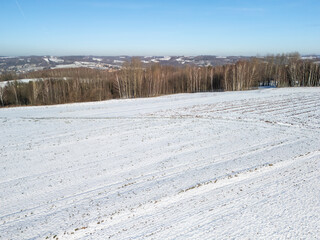 A serene winter landscape featuring snow-covered fields and sparse trees under a clear blue sky, evoking a sense of tranquility and natural beauty.