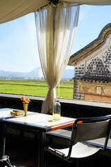 A serene outdoor café with a stunning countryside view, featuring a table set with a glass bottle of lemon water, a drinking glass, and a small flower vase. 