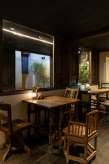 A cozy and atmospheric café at night, featuring rustic wooden tables and chairs illuminated by warm lantern light. The setting exudes a vintage charm with wooden window frames, textured walls, 