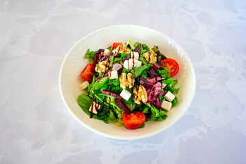 Green salad with arugula, lamb and tomatoes. Healthy vegan dish. Top view at table. Turkish Coban (choban) salata or Shepherds salad, Akdeniz salad in white bowl.