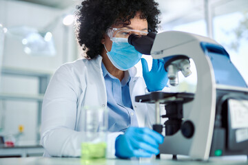 Multiracial female scientist looking through microscope while working on medical research in a...