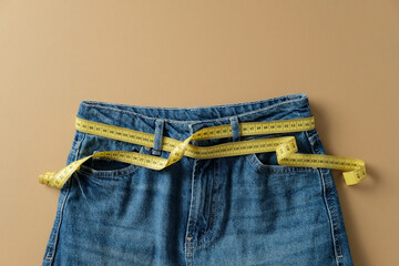 Blue jeans and yellow measuring tape on a brown background. Weight loss concept