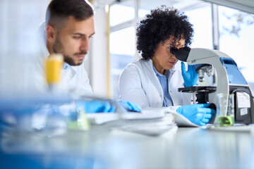 Multiracial female scientist looking through a microscope whit her male colleague in laboratory.	