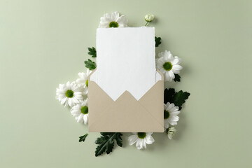 Beige envelope with blank card mockup surrounded by white daisy flowers on light green background. Perfect for wedding invitations, greeting cards.