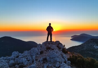 A man stands on a rocky hill overlooking a body of water