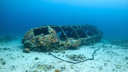 Fototapeta premium Explore the mysterious depths with this stunning image of a sunken ship covered in colorful coral reefs and tangled anchor chains