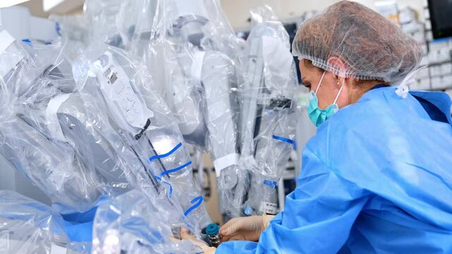 Female doctor attaches robotic manipulator arm to the surgical device input into patient's abdomen. Performance of minimal invasive operation.