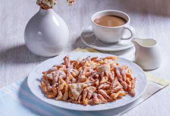 Traditional Maslenitsa dessert angel wings served with coffee on a light background.