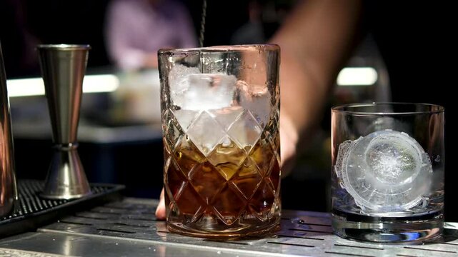 Close up of a professional bartender is mixing an alcoholic cocktail with professional crystal long lasting ice cubes to customers at the bar or disco club. Professional bartender masterly creating