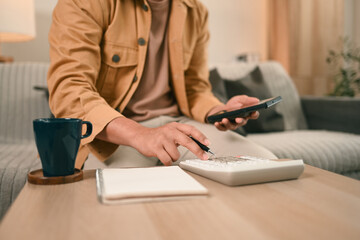 A Close-up of a man in a casual outfit calculates expenses using a calculator, Taking control of...