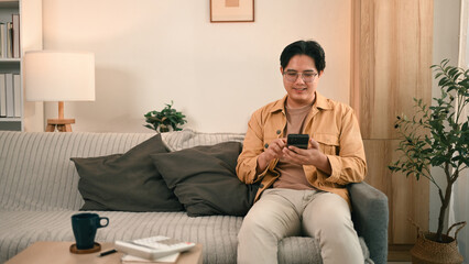 A man in a casual outfit sits on a cozy couch, checking finances on his smartphone, symbolizing digital banking and home finance planning, Digital financial management made easy