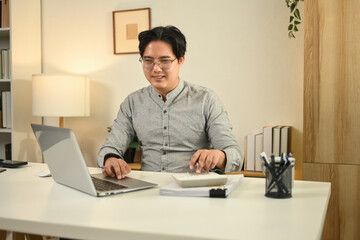 Obraz premium A professional accountant working on a laptop and calculator, reviewing financial documents in a modern office, symbolizing business analysis, financial planning, and corporate accounting