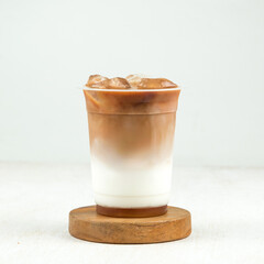 Enjoying a refreshing iced coffee layered with cream and brewed coffee, presented elegantly in a clear cup on a wooden base