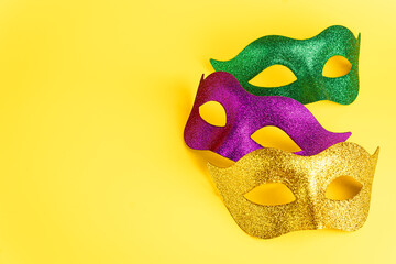 Three glittering masks in purple, green, and gold arranged on a vibrant yellow background, evoking...