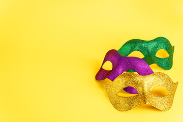 Three glittering masks in purple, green, and gold arranged on a vibrant yellow background, evoking...