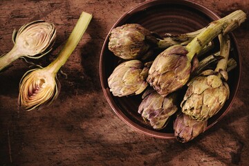 Artichokes rest in a rustic bowl on a wooden surface, showcasing their unique shapes and earthy colors. This moment embodies the essence of farm-to-table philosophy, celebrating slow cooking