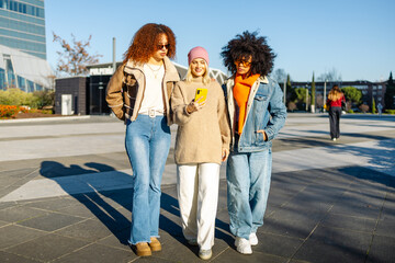 Three friends enjoying time outdoors together and using smartphone while walking.