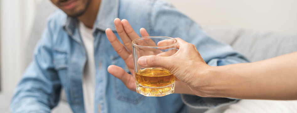 Alcoholism, depressed asian young man refuse, push out alcoholic beverage glass, drink whiskey, sitting alone at night. Treatment of alcohol addiction, having suffer abuse problem alcoholism concept.