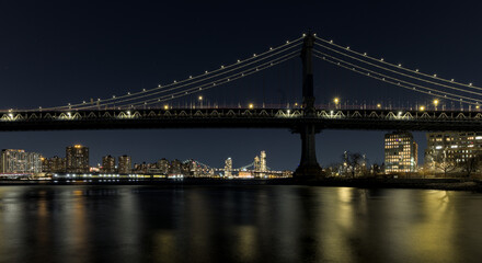 Fototapeta premium manhattan bridge detail long exposure at night with east river reflections and williamsburg bridge in the background (train passing walkway overpass) dumbo brooklyn travel tourism usa nyc landmark