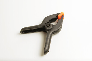 Close-up of a black plastic spring clamp with orange tips, commonly used to clamp paper, photo and backdrops for photography. 