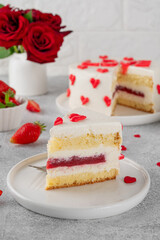 Vanilla strawberry cake with small red hearts for Valentine's day on a white plate on a gray concrete background. Romantic cake.