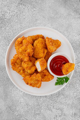 Crispy chicken nuggets with ketchup on a white plate on a gray concrete background.