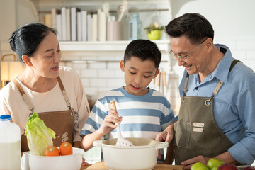 Asian grandparents support and help grandson cooking breakfast in the kitchen. Grandmother and grandfather watching nephew learning skill on morning weekend. Family love and bonding.