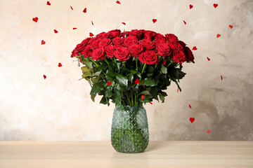Bouquet of beautiful red roses in vase on table under falling heart-shaped confetti