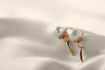 Beautiful pearl earrings on white silk, closeup. Space for text