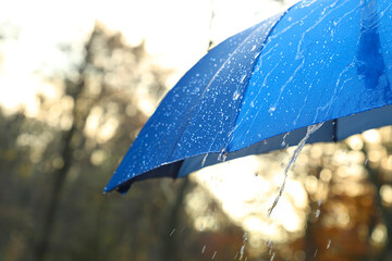 Open blue umbrella under pouring rain outdoors, closeup