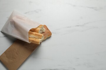 Paper bags with fresh baguette and ciabatta on white marble table, top view. Space for text