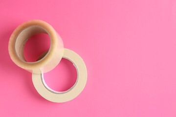 Rolls of adhesive and masking tapes on pink background, top view. Space for text