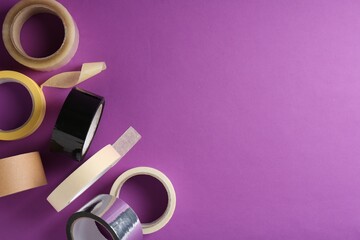 Rolls of different adhesive tapes on purple background, flat lay. Space for text