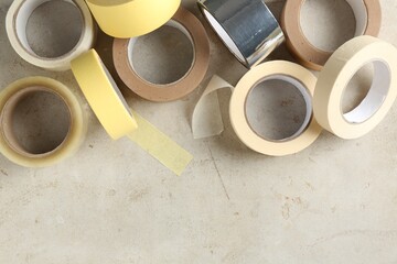 Rolls of different adhesive tapes on light grey table, flat lay. Space for text
