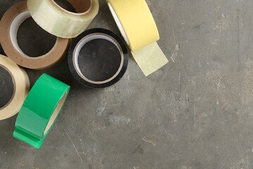 Rolls of different adhesive tapes on grey table, flat lay. Space for text