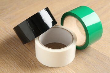 Rolls of different adhesive tapes on wooden table, closeup