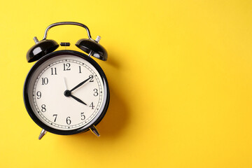 Black alarm clock on yellow background, top view. Space for text