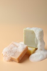 Soap bars with foam on beige background, closeup. Space for text