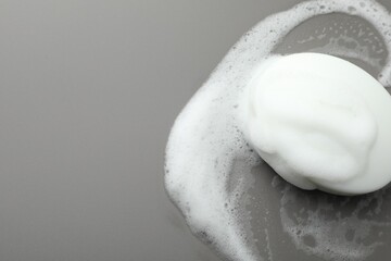 Soap bar with foam on grey background, top view. Space for text