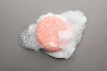Soap bar with foam on grey background, top view