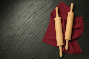 Wooden rolling pins and napkin on dark gray textured table, flat lay. Space for text