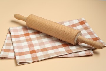 Wooden rolling pin and checkered napkin on beige background