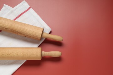 Wooden rolling pins and napkin on red background, flat lay. Space for text