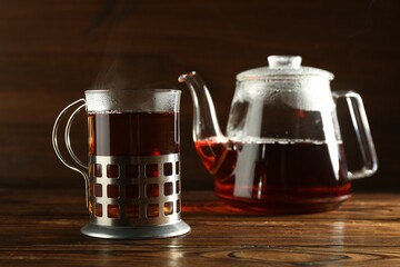 Glass of hot tea in holder and teapot on wooden table