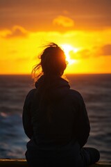 Woman in silhouette gazing at a fiery sunset over the ocean feeling pensive and reflective